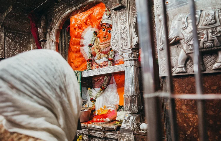 A pilgrim in a white head covering before a garlanded Devi shrine
