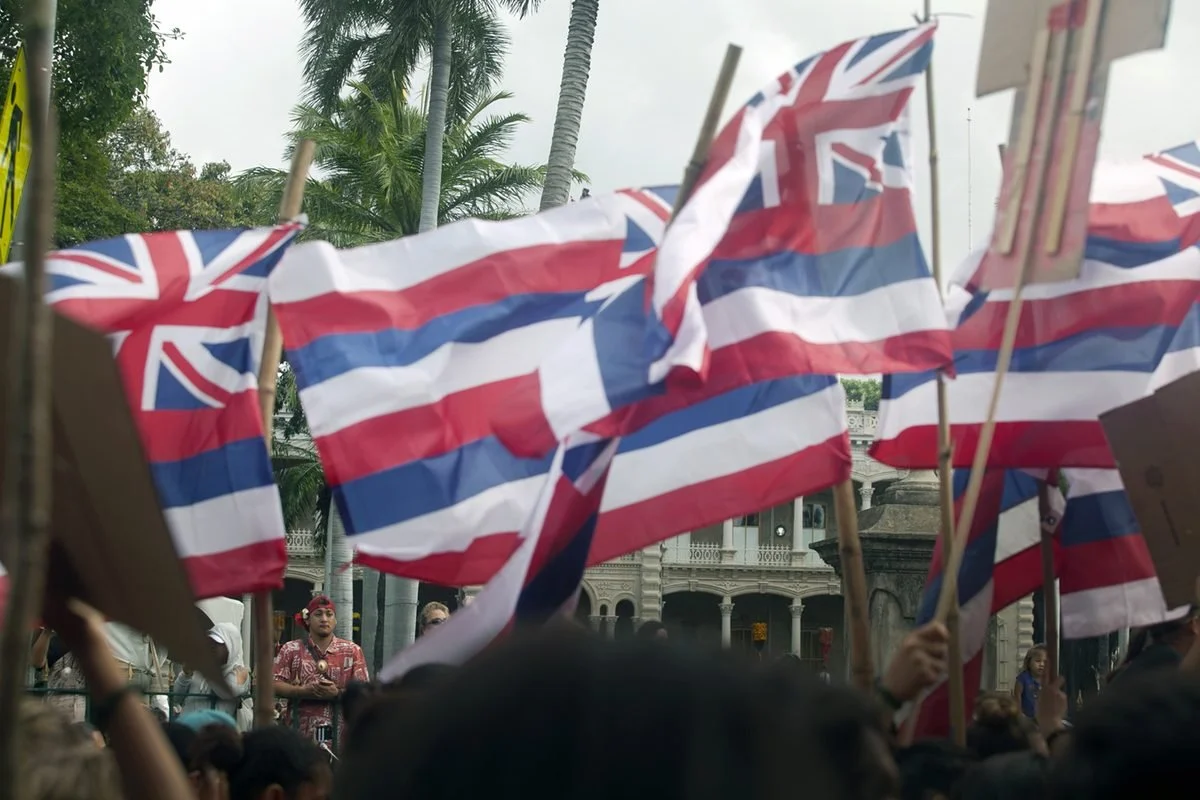 Community members holding Hawaiian flags at a gathering in front of ʻIolani Palace