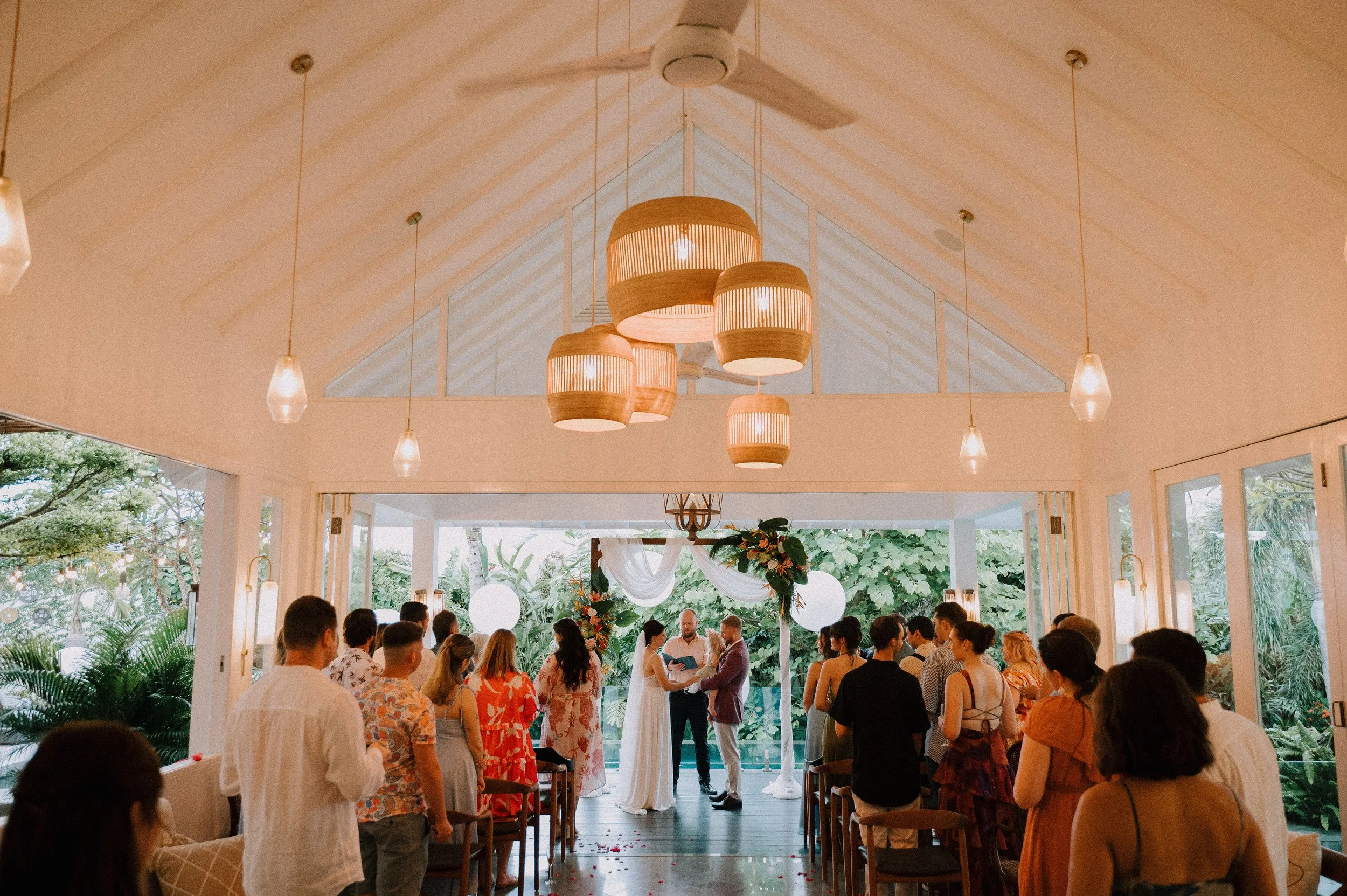 A couple exchanging vows beneath the floral arch, surrounded by their guests