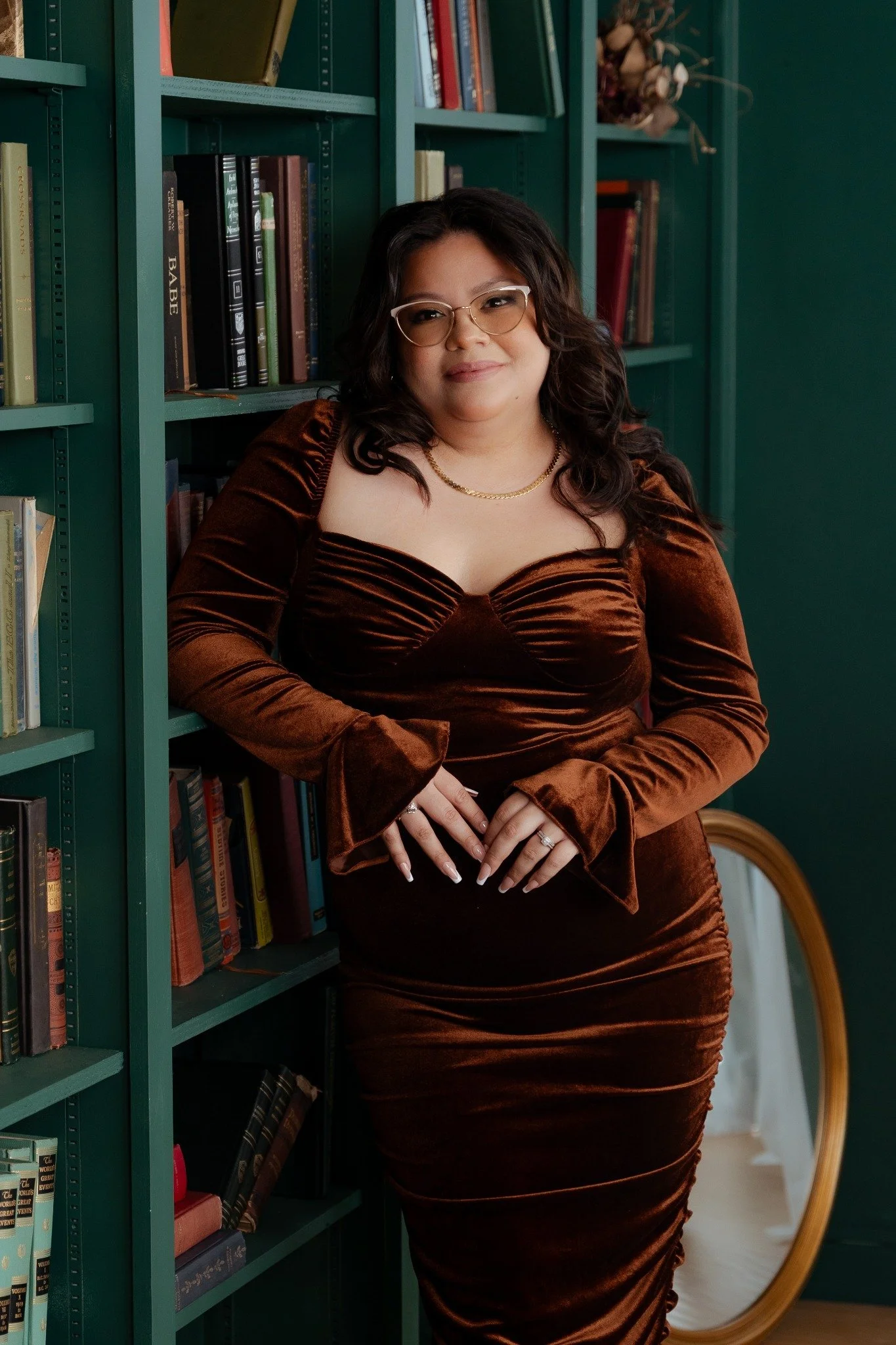 A woman in a brown velvet dress posing beside a green window frame.