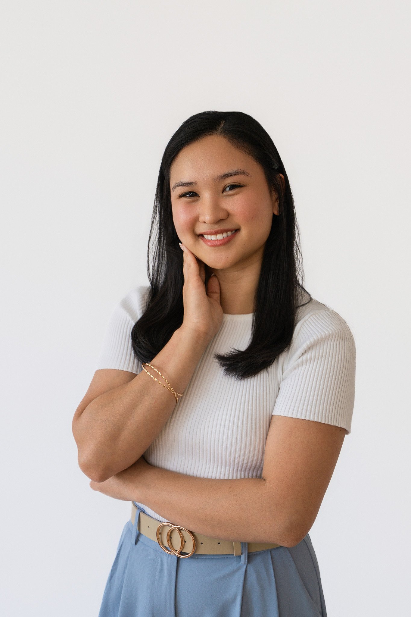 A smiling woman in a white shirt resting her hand against her cheek.