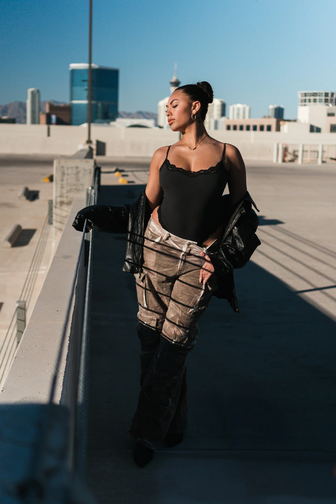 Editorial fashion portrait of a woman in a black outfit and patterned skirt on a rooftop beneath a blue sky.