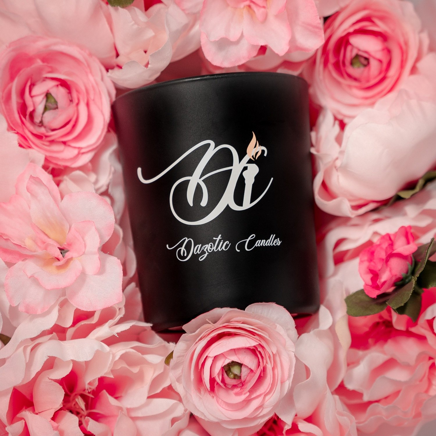 A black branded candle surrounded by pink roses.