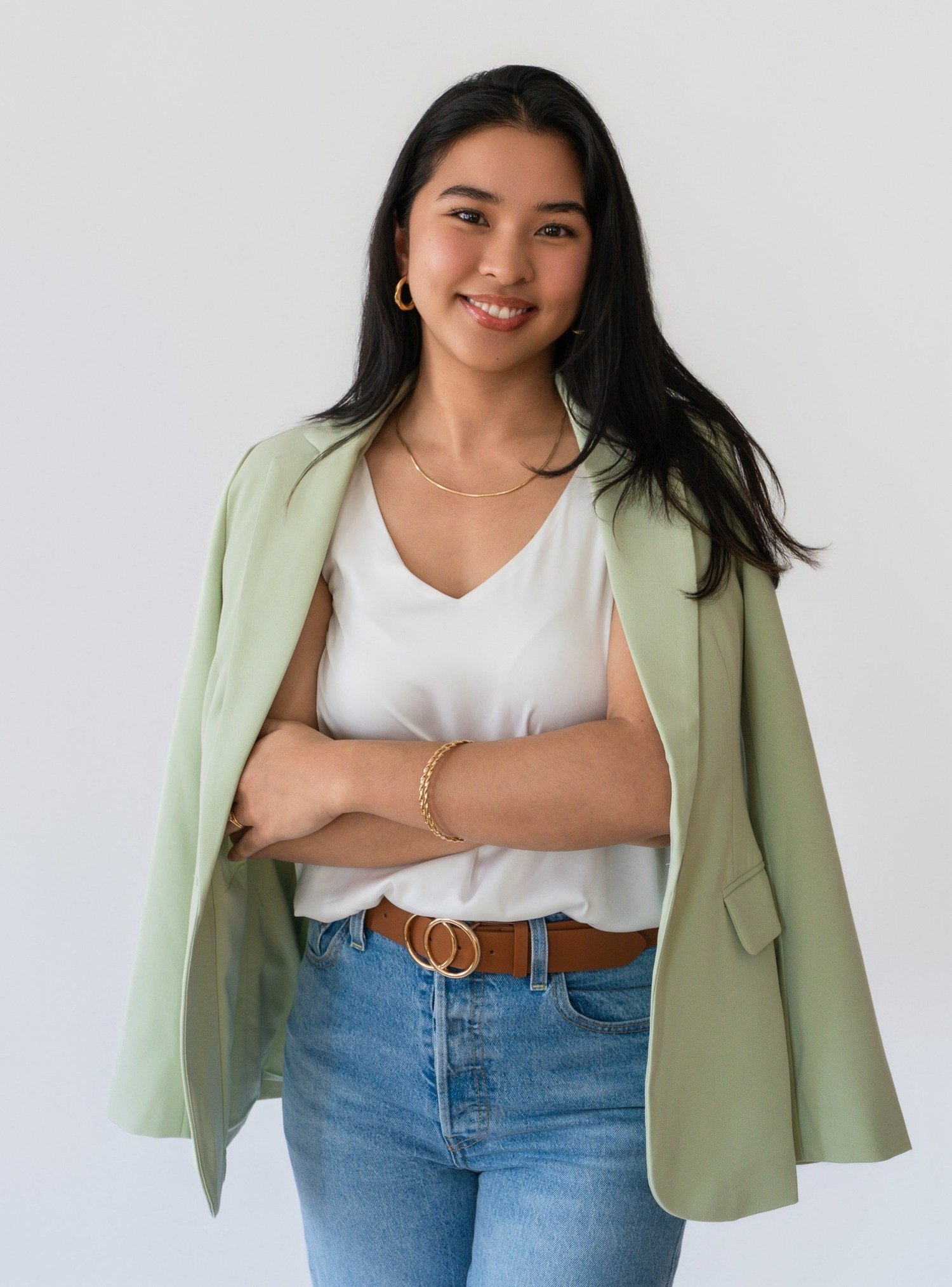 A woman in a green blazer and white top smiling with her arms crossed.
