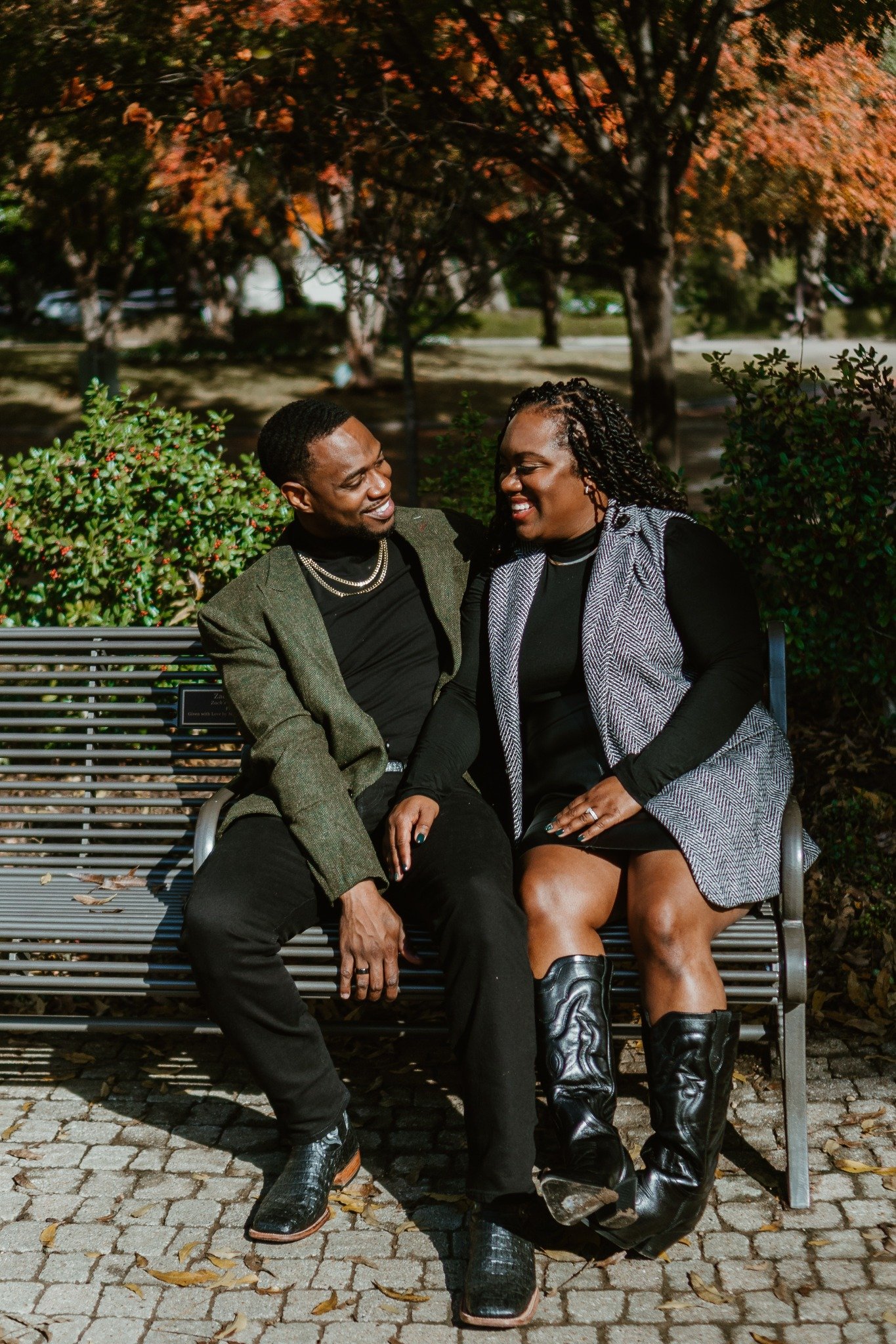 A couple sitting together on a park bench beneath autumn leaves.