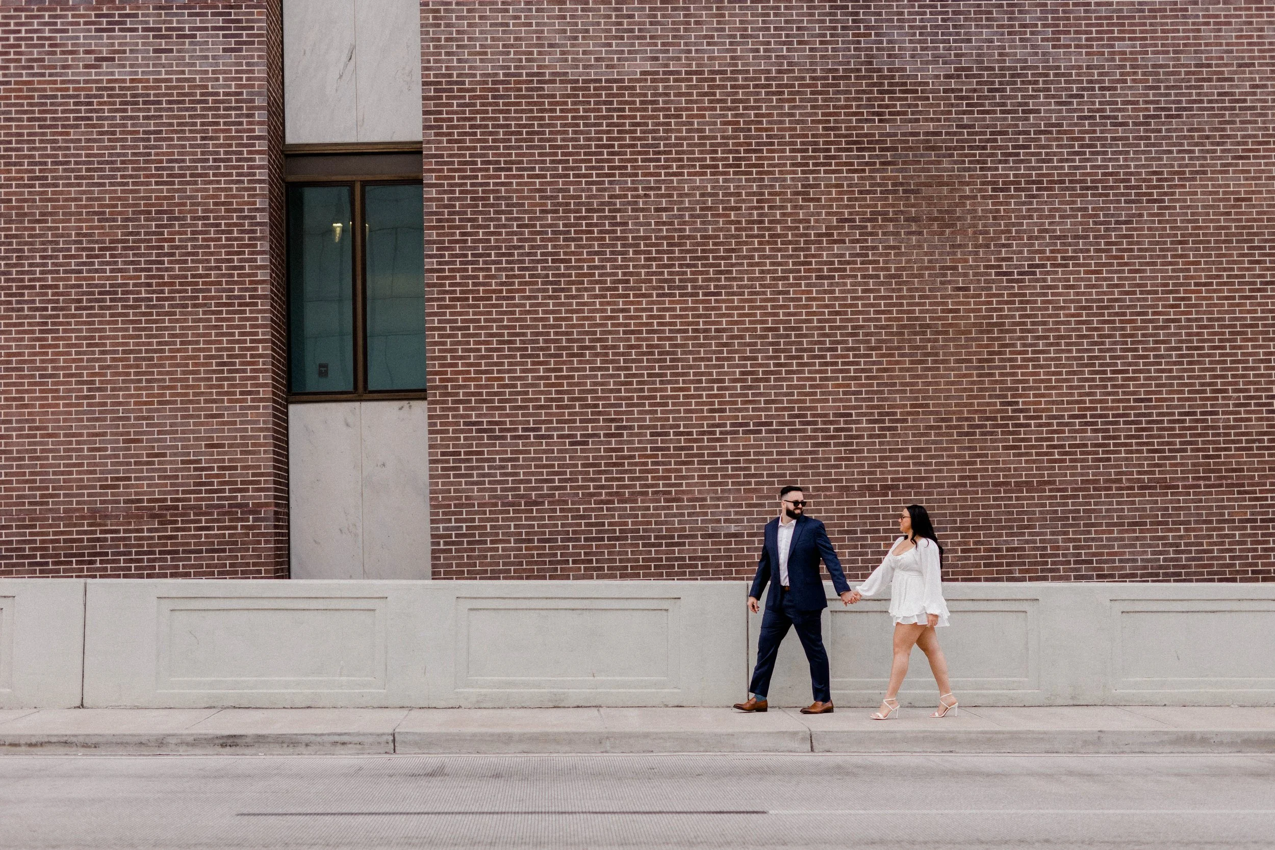 A couple walking together past a brick wall