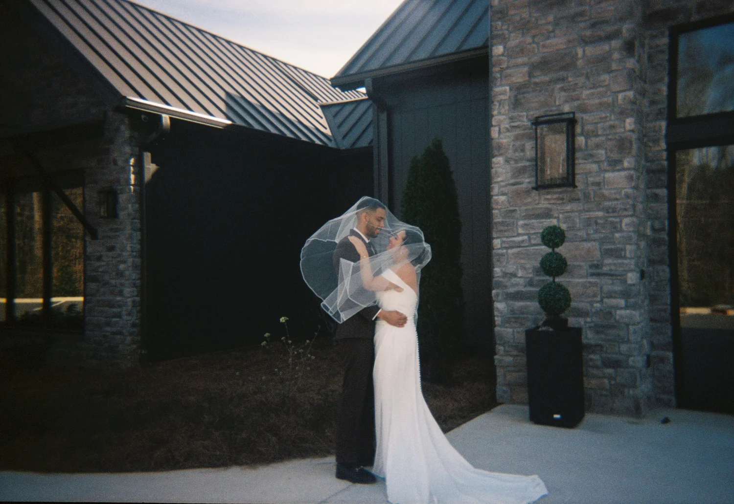 A bride in a stone doorway with her veil lifting, shot on 35mm film
