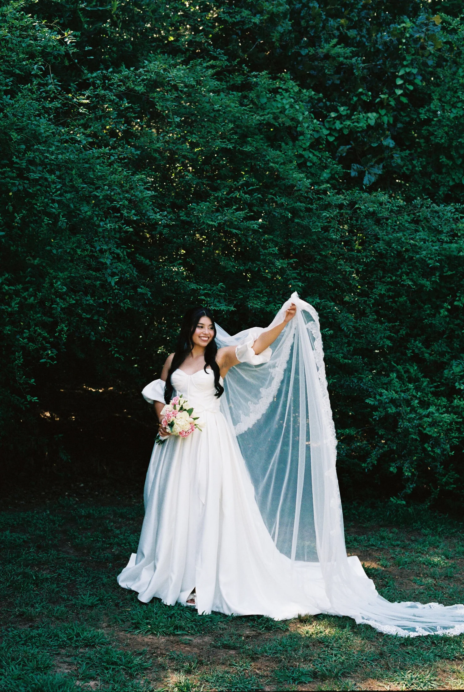 A bride lifting her veil in front of the greenery, shot on 35mm film