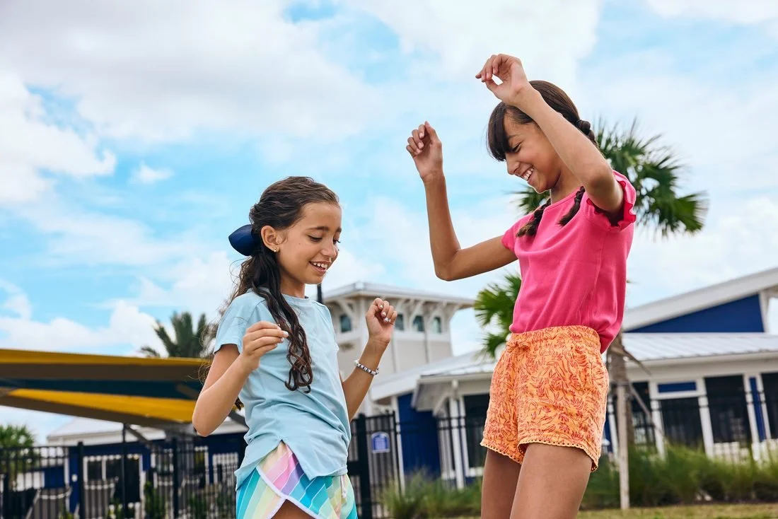 Two girls dance outdoors in front of a blue clubhouse.