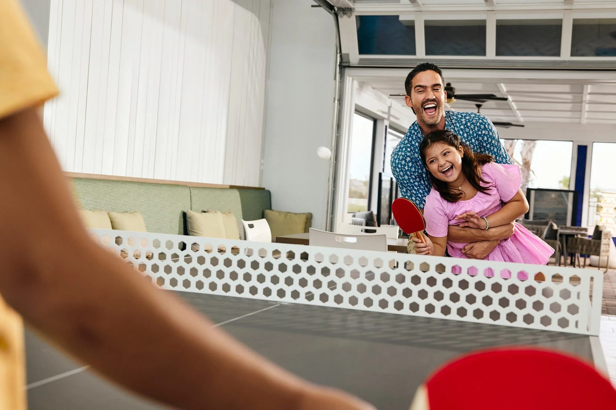 A father hugs his laughing daughter during a ping-pong game at the clubhouse.