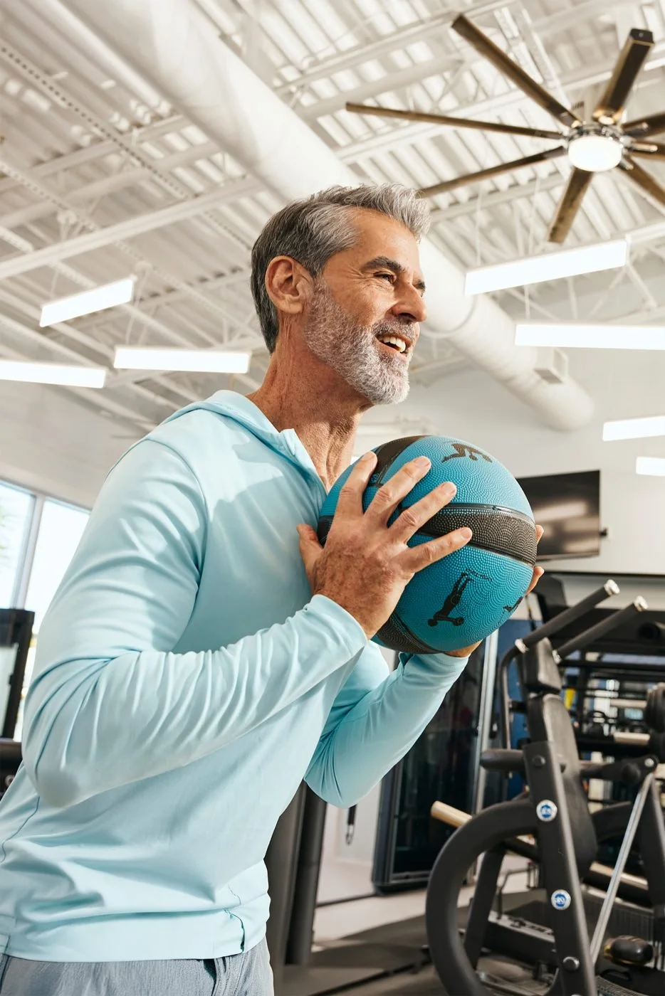 A man grins as he readies a medicine ball in a clubhouse fitness center.