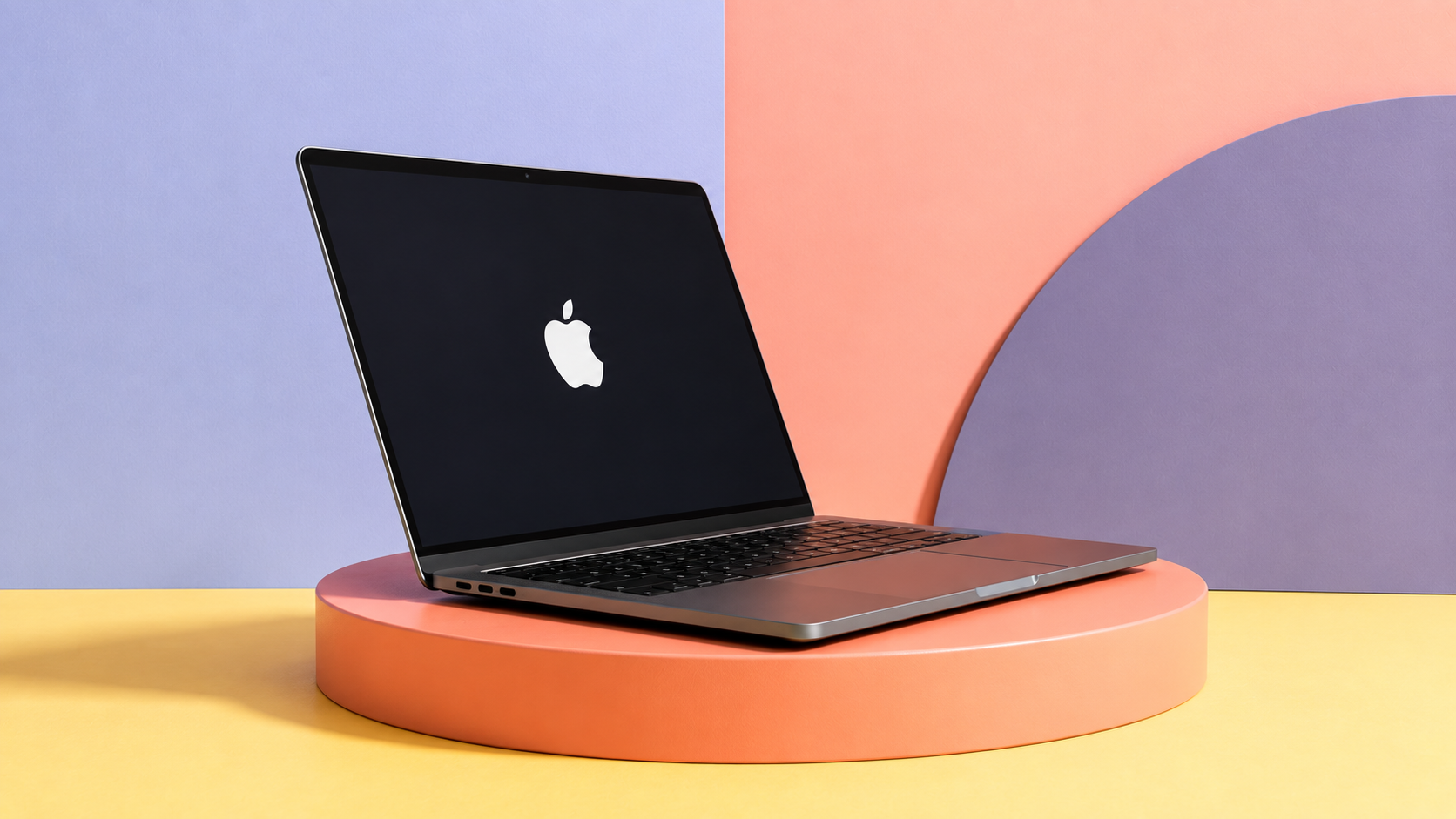 MacBook aperto di tre quarti su un podio arancione, con sfondo pastello