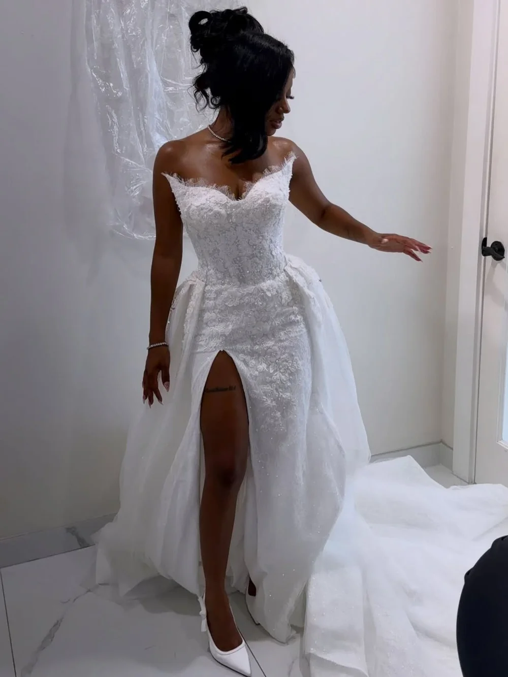 Alize trying on her custom strapless lace wedding gown with a high slit and long overskirt train, designed by Estelle Bridal