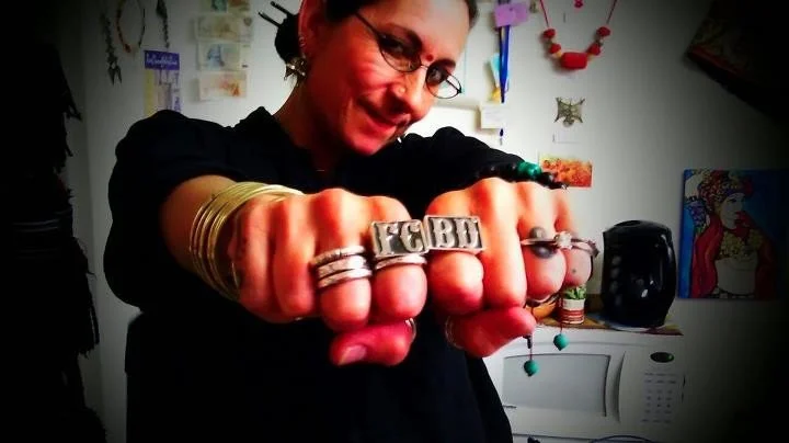 Carolena Nericcio holding out her fists toward the camera, wearing rings that spell FCBD across her knuckles