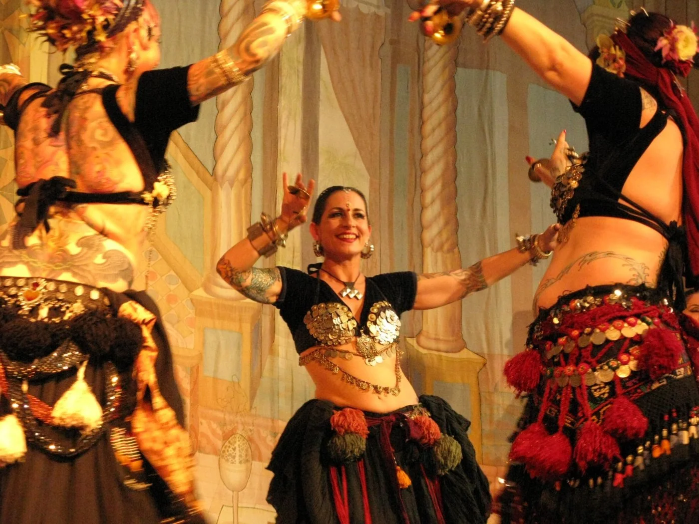 Carolena Nericcio smiling on stage with zills, dancing FCBD® Style with two dancers framing her