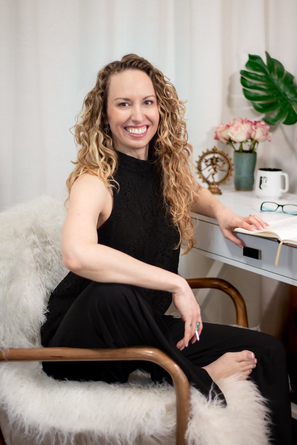 DeAnna Freeman smiling at her desk, seated in a chair draped with a white sheepskin