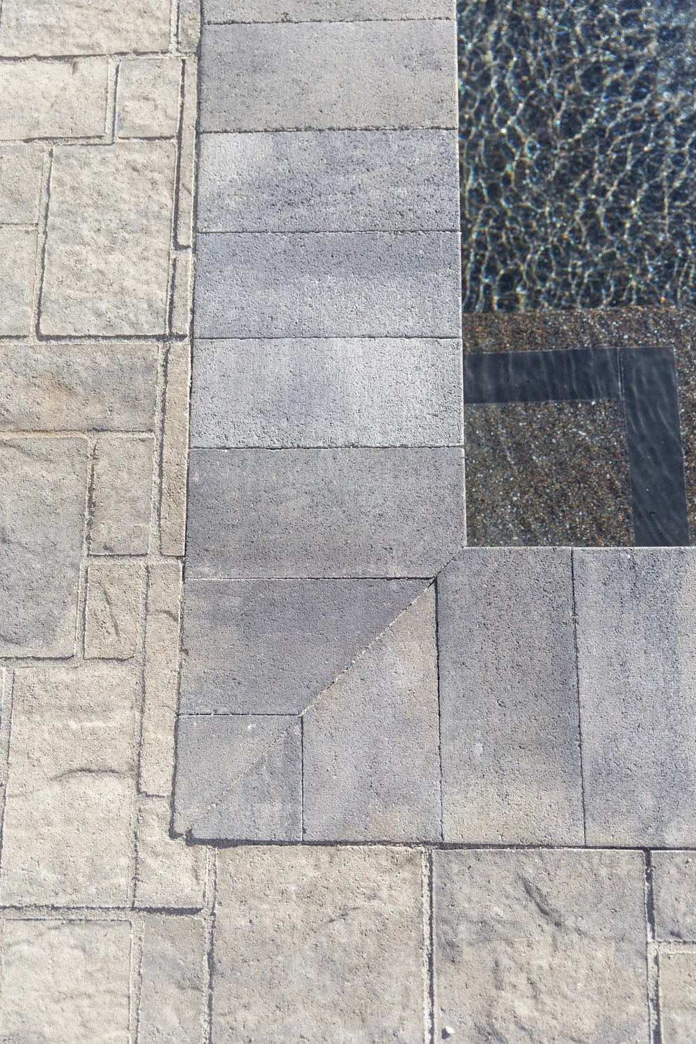 Gray pool coping and patterned paver deck beside the water.