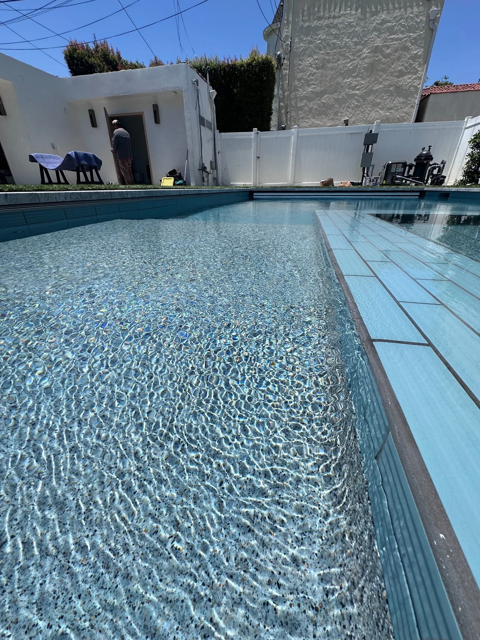 Sunlight rippling across a pebble-textured shallow pool surface beside pale rectangular tile.