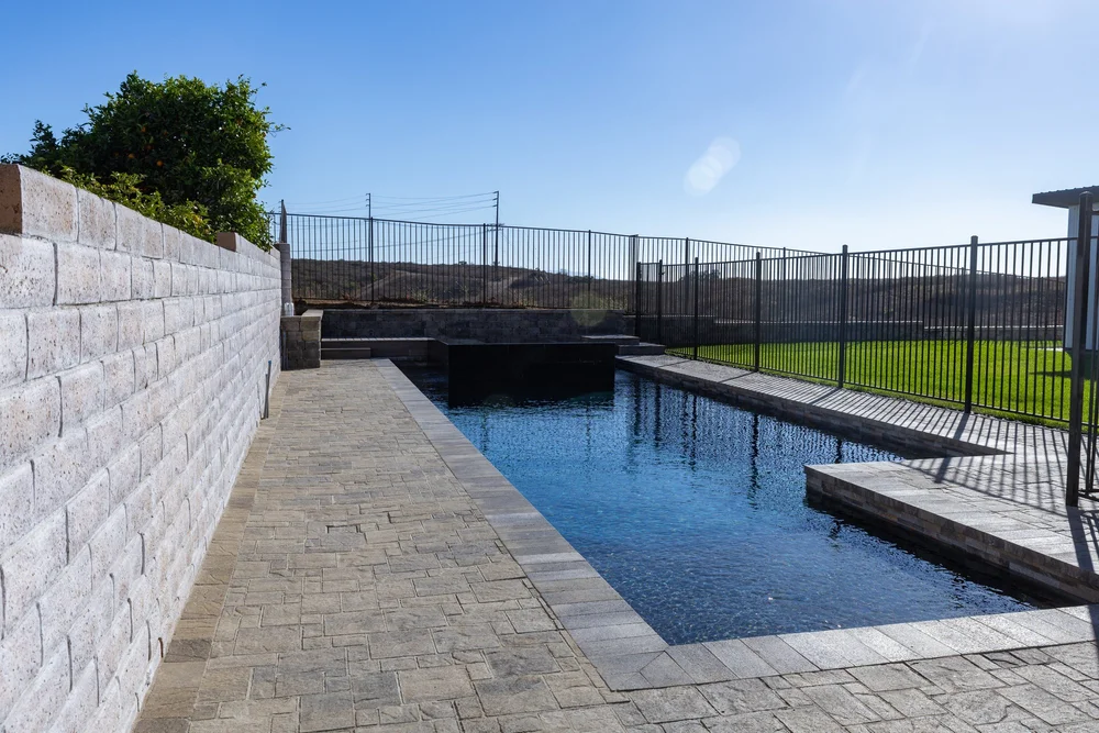 Rectangular blue pool with gray coping, a paved deck and a raised square spa.