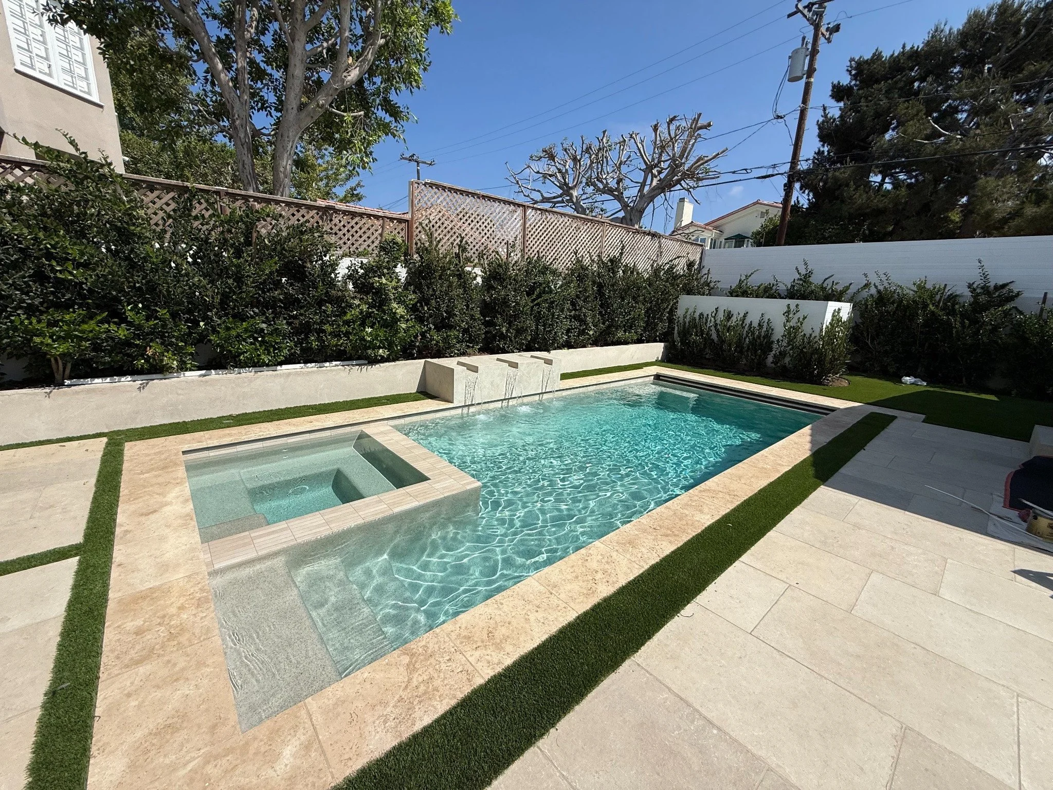 Hansen rectangle pool with a square spa, beige coping, and three water spills