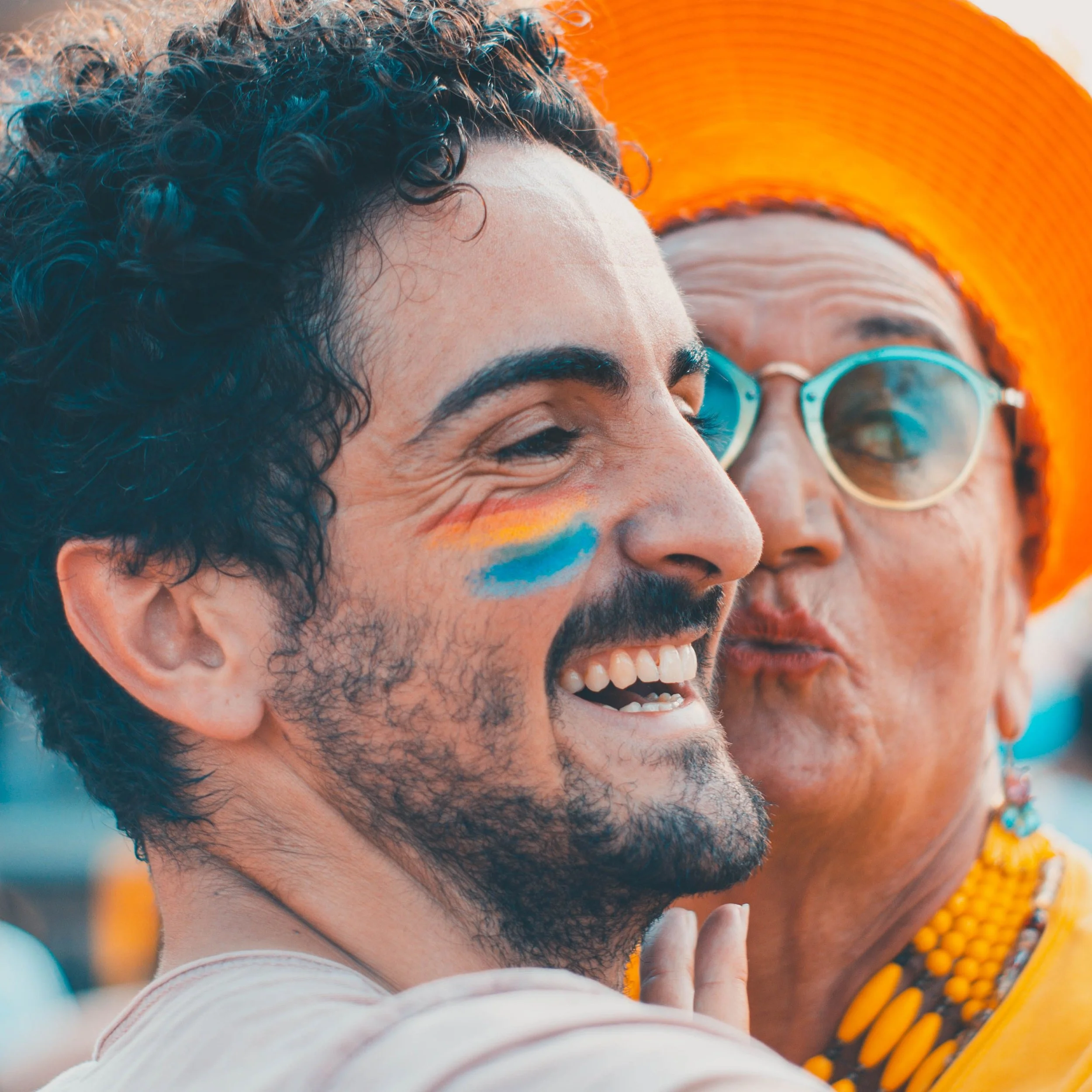 A man and an older woman share a joyful moment outdoors, smiling with painted faces and bright clothing. Credit: Photo by Dario Moscato from Pexels.