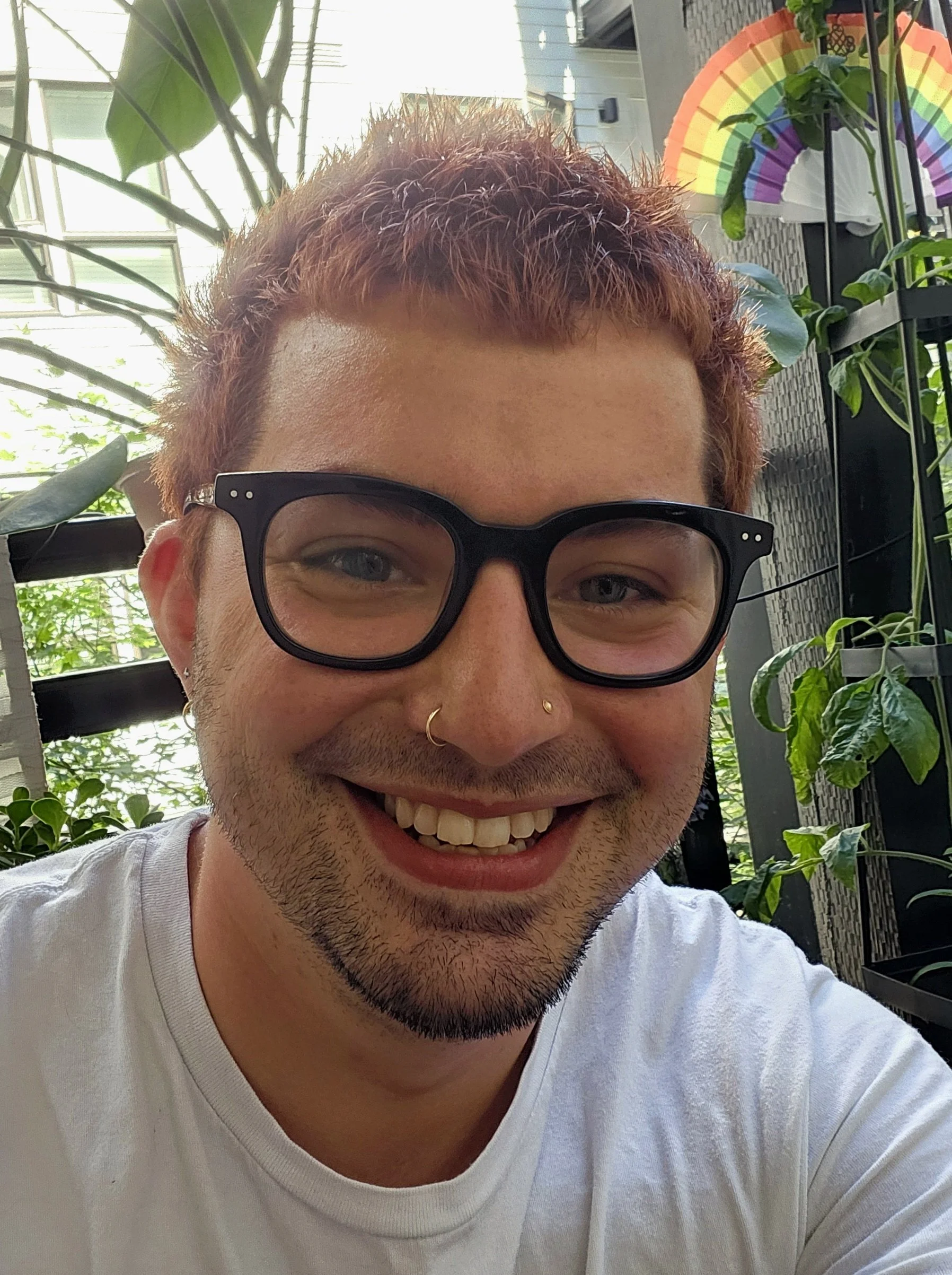 Ryan smiling in a close-up photo with plants and a rainbow decoration in the background.