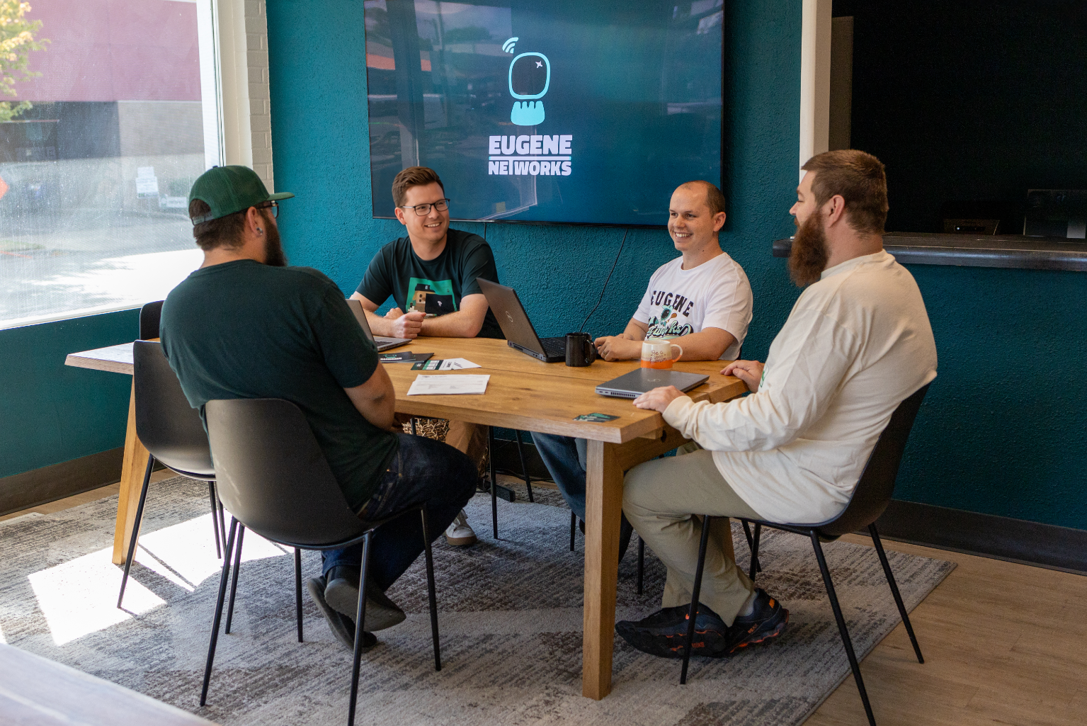 Four Eugene Networks engineers talking together around a table in the Eugene office