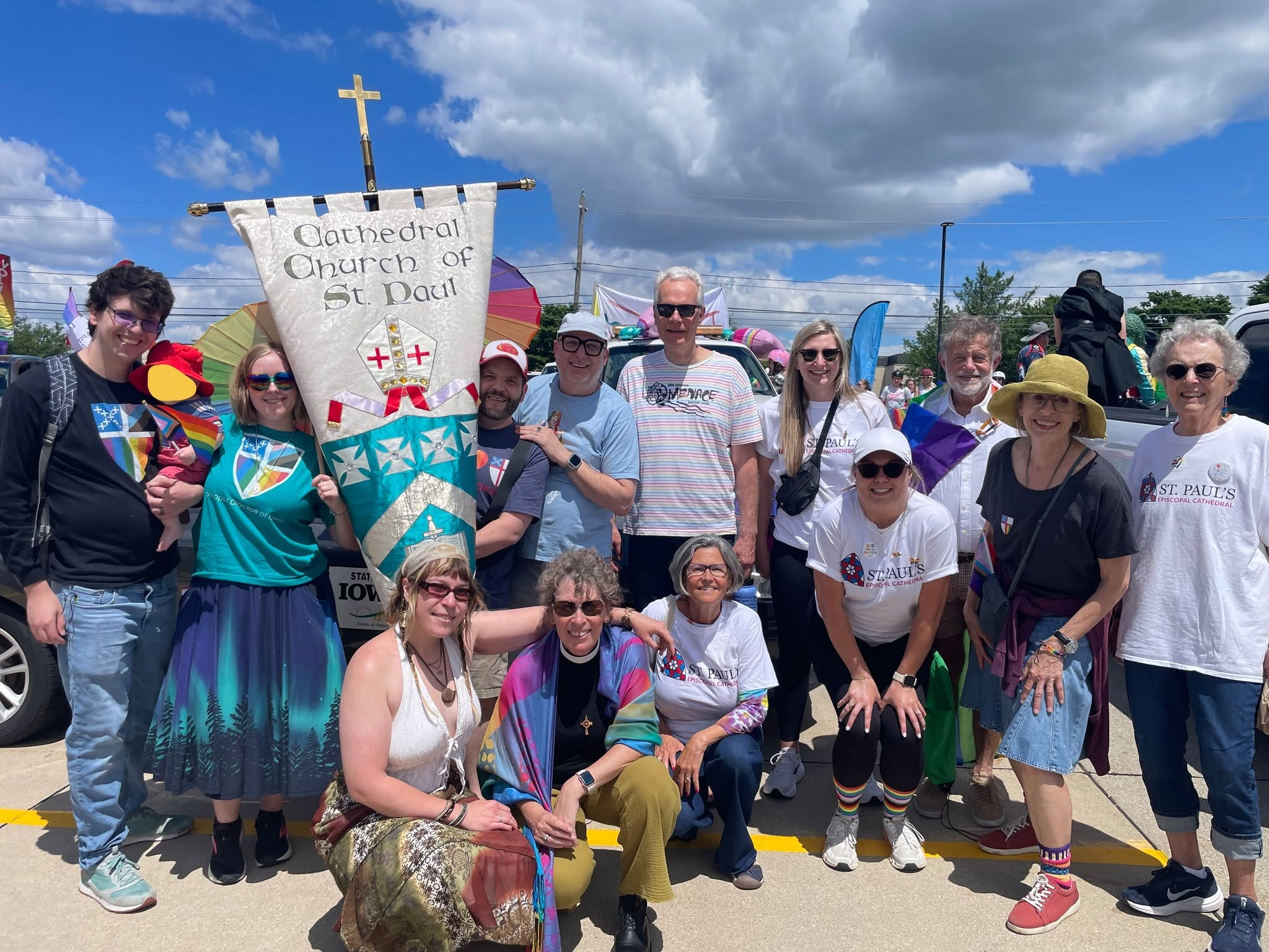 A smiling group gathered outdoors with the Cathedral Church of St. Paul banner and colorful flags