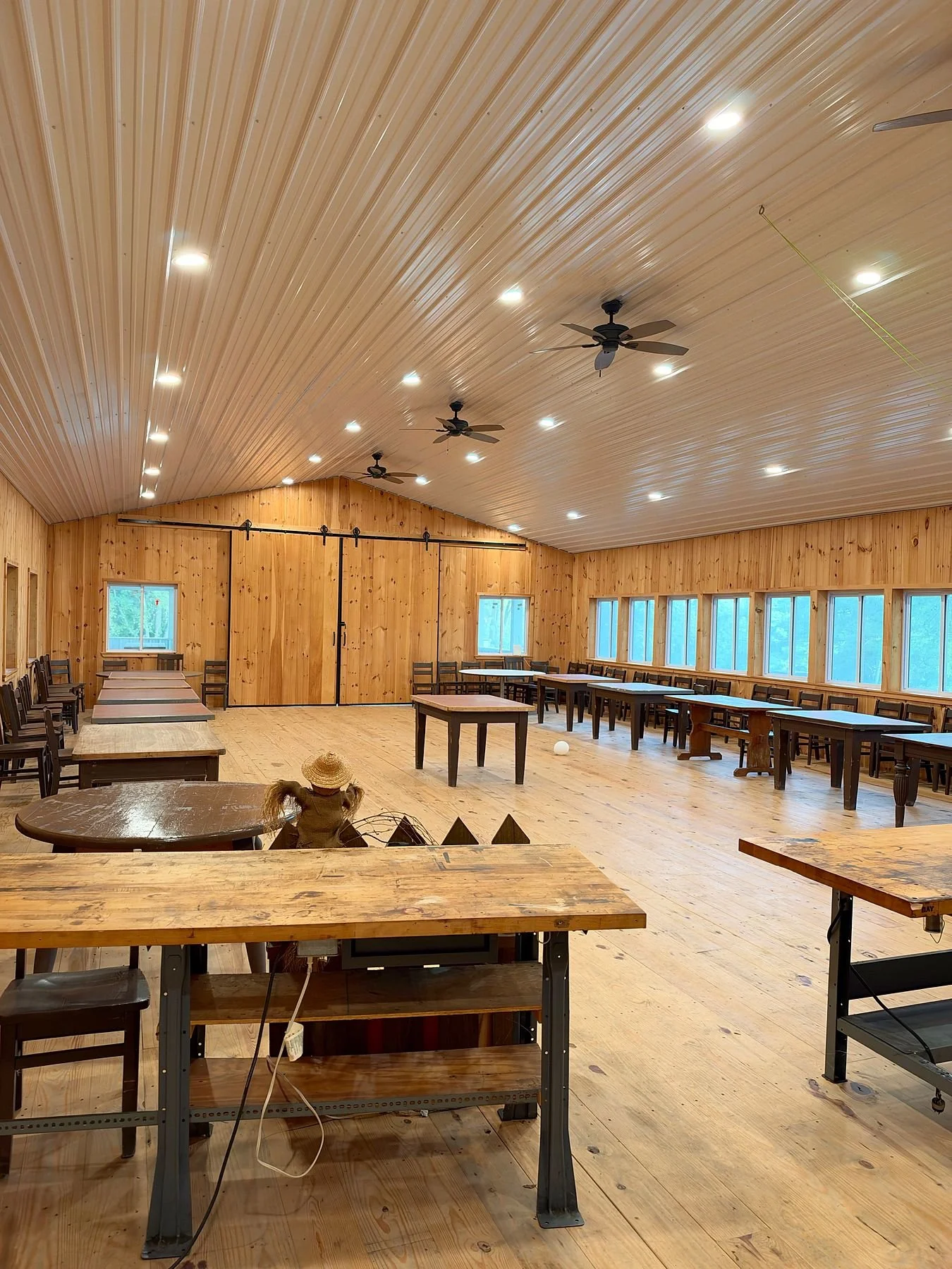 Inside the barn hall, with wood walls, tables and chairs, and ceiling fans