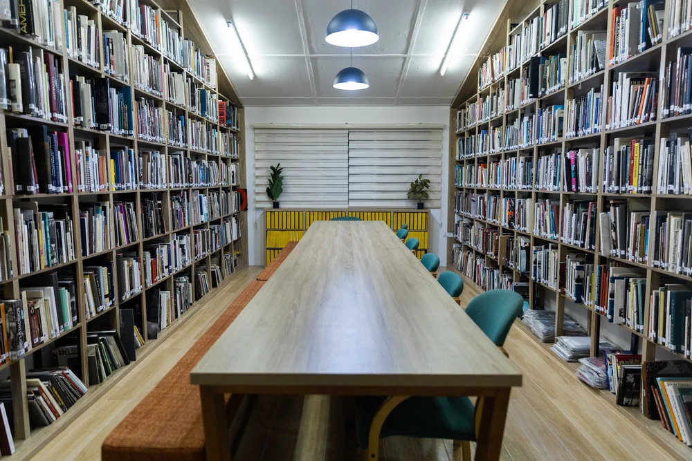 Library shelves alongside a long reading table with hanging lamps.