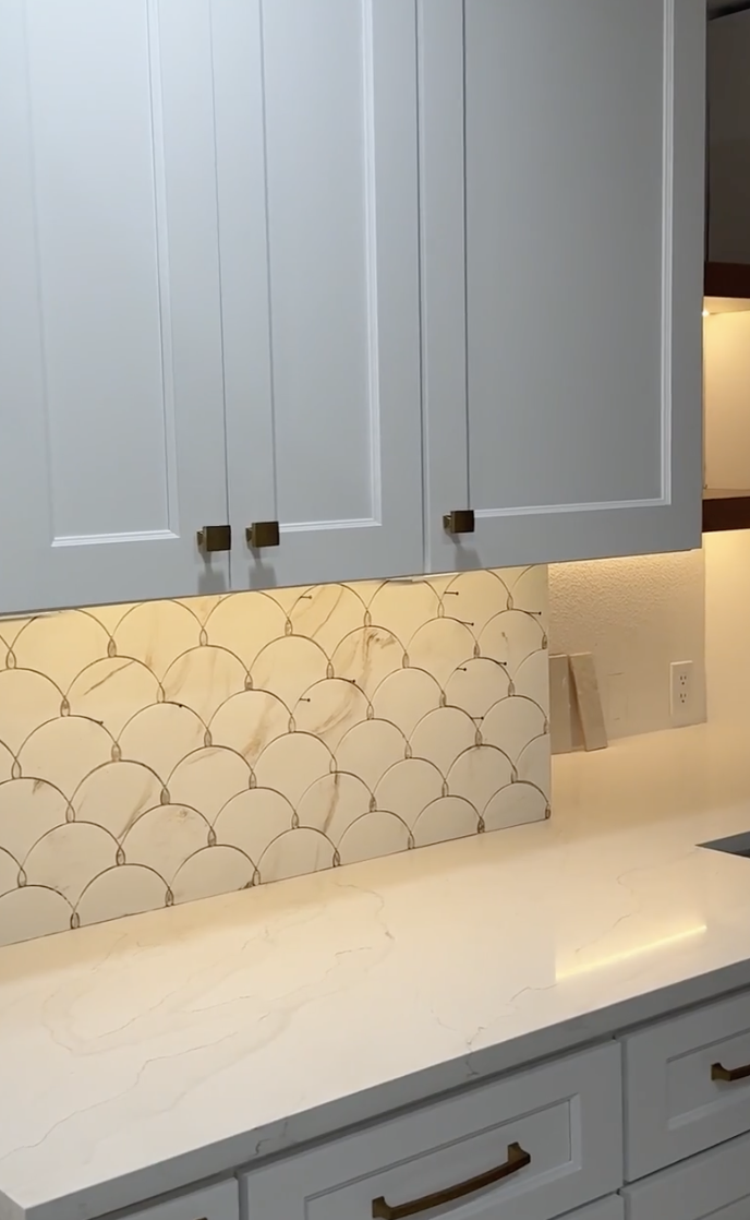 Scalloped tile backsplash with white cabinetry and under-cabinet lighting