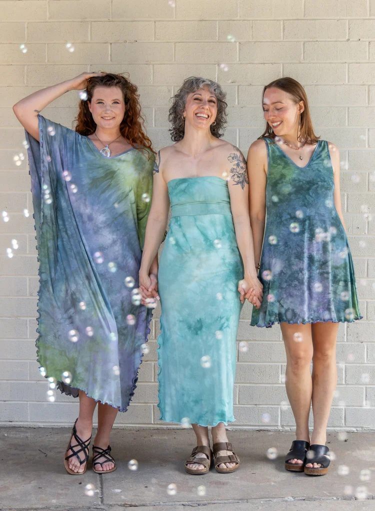 Three women laughing in hand-dyed dresses as soap bubbles drift around them