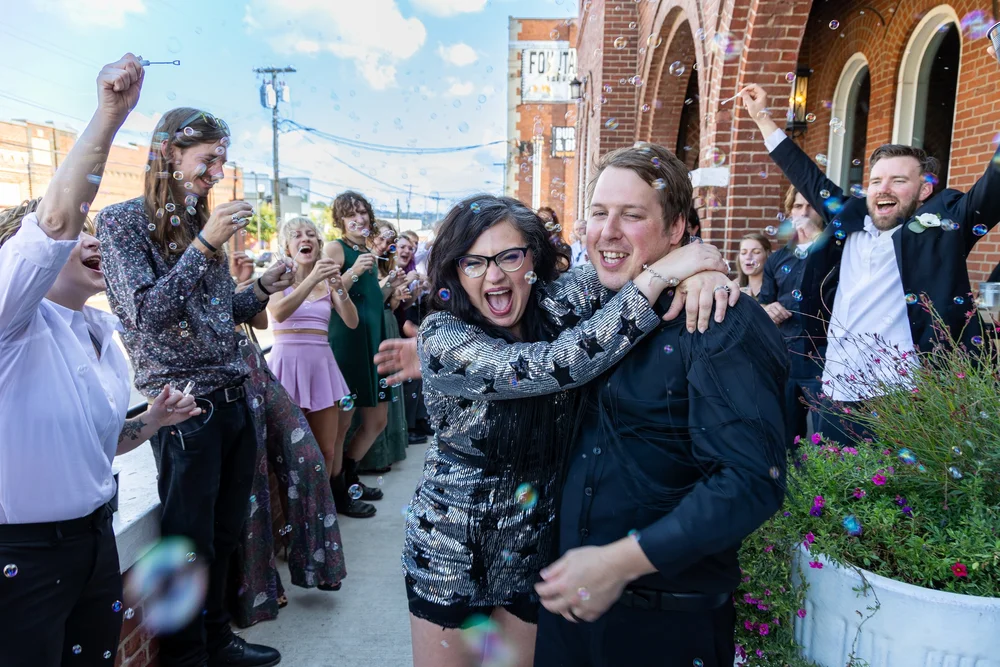 Bride and groom laughing during a bubble send-off as guests cheer