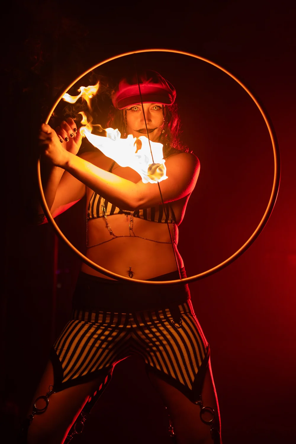 Fire performer spinning a flaming hoop under red light