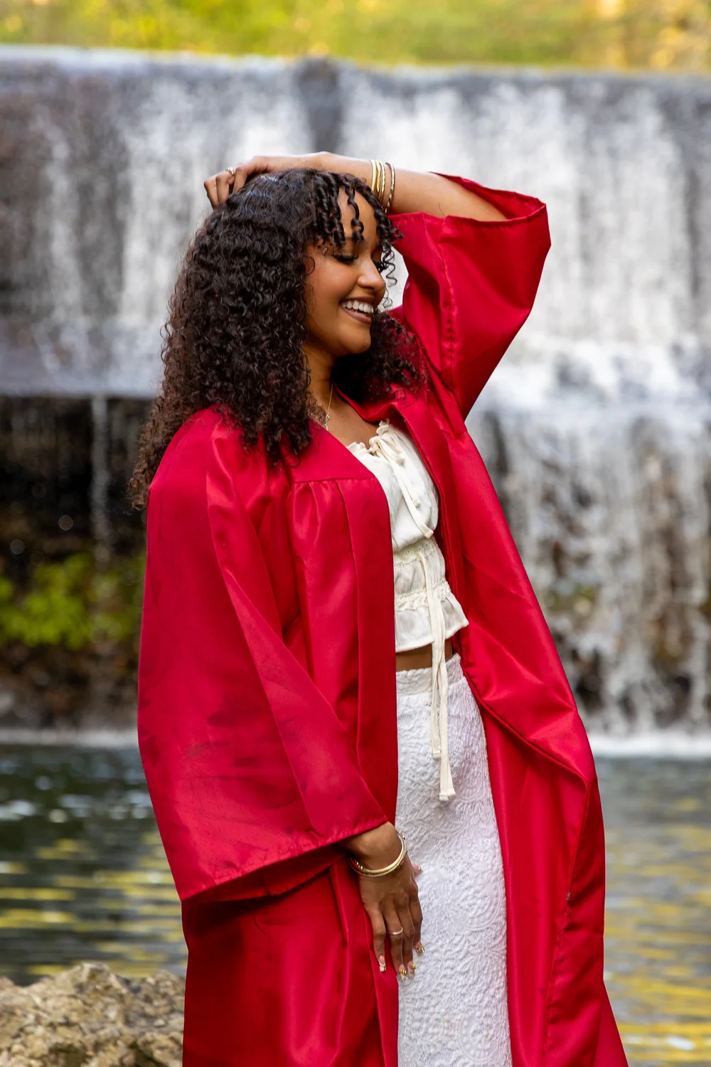 Graduate in a red gown standing before a waterfall