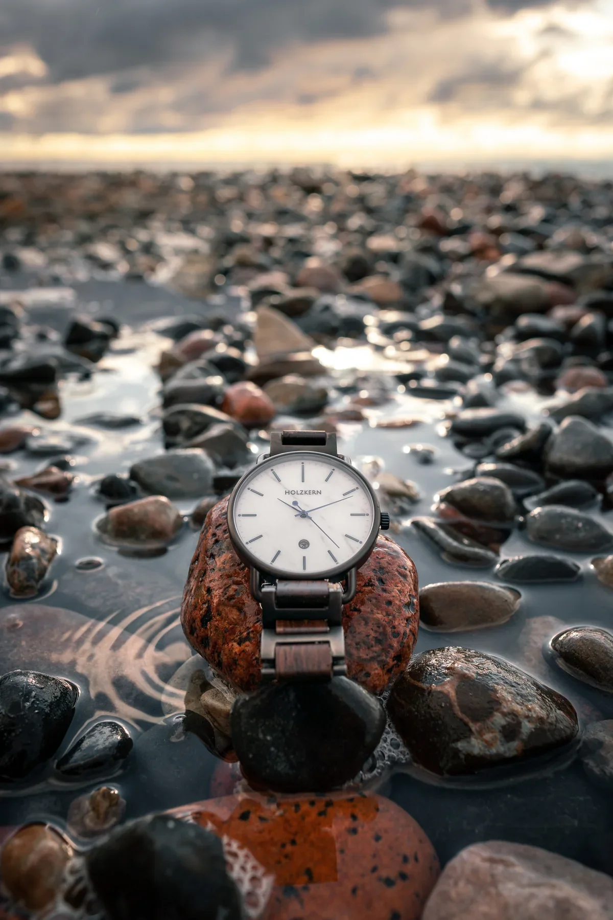 Holzkern watch photographed beside water and shoreline stones