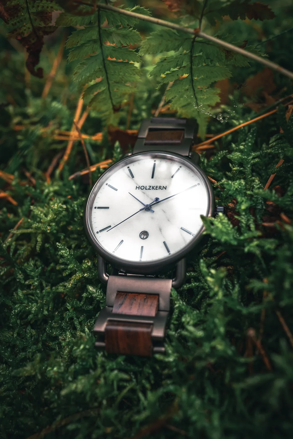 White-dial Holzkern watch resting among deep green forest textures