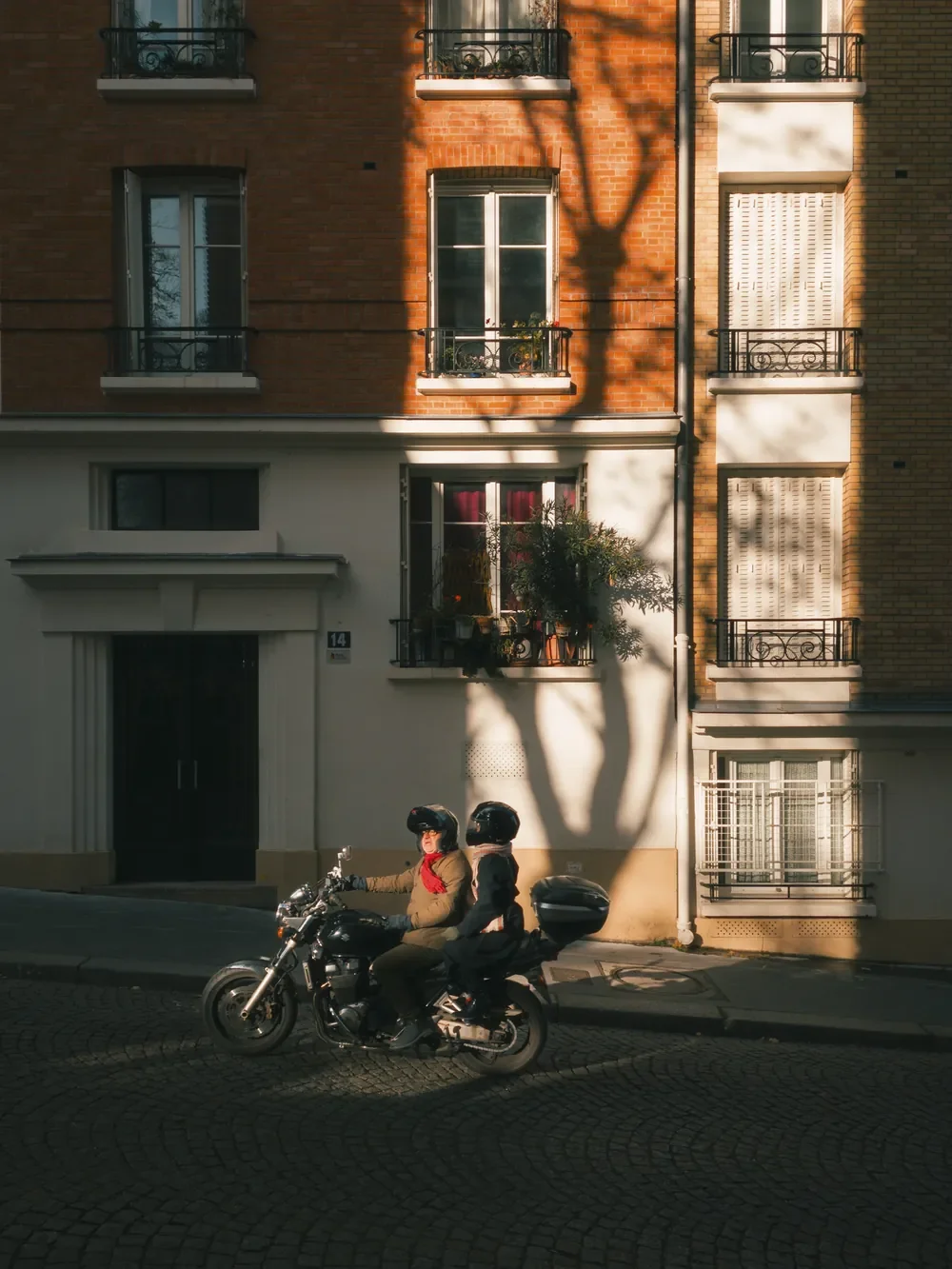Two people on a motorcycle passing through winter sunlight