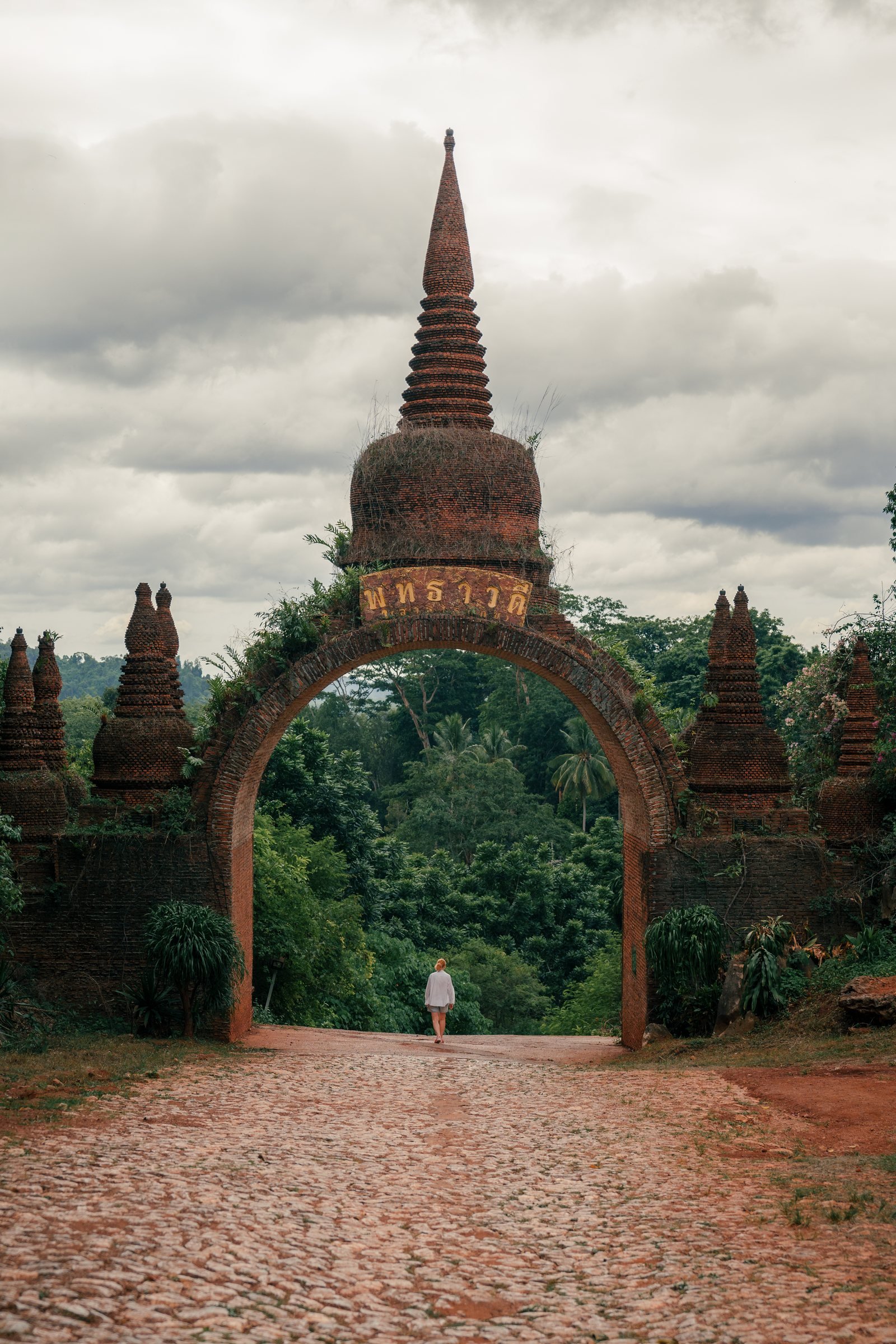 Traveller walking beneath a historic brick gateway in Thailand