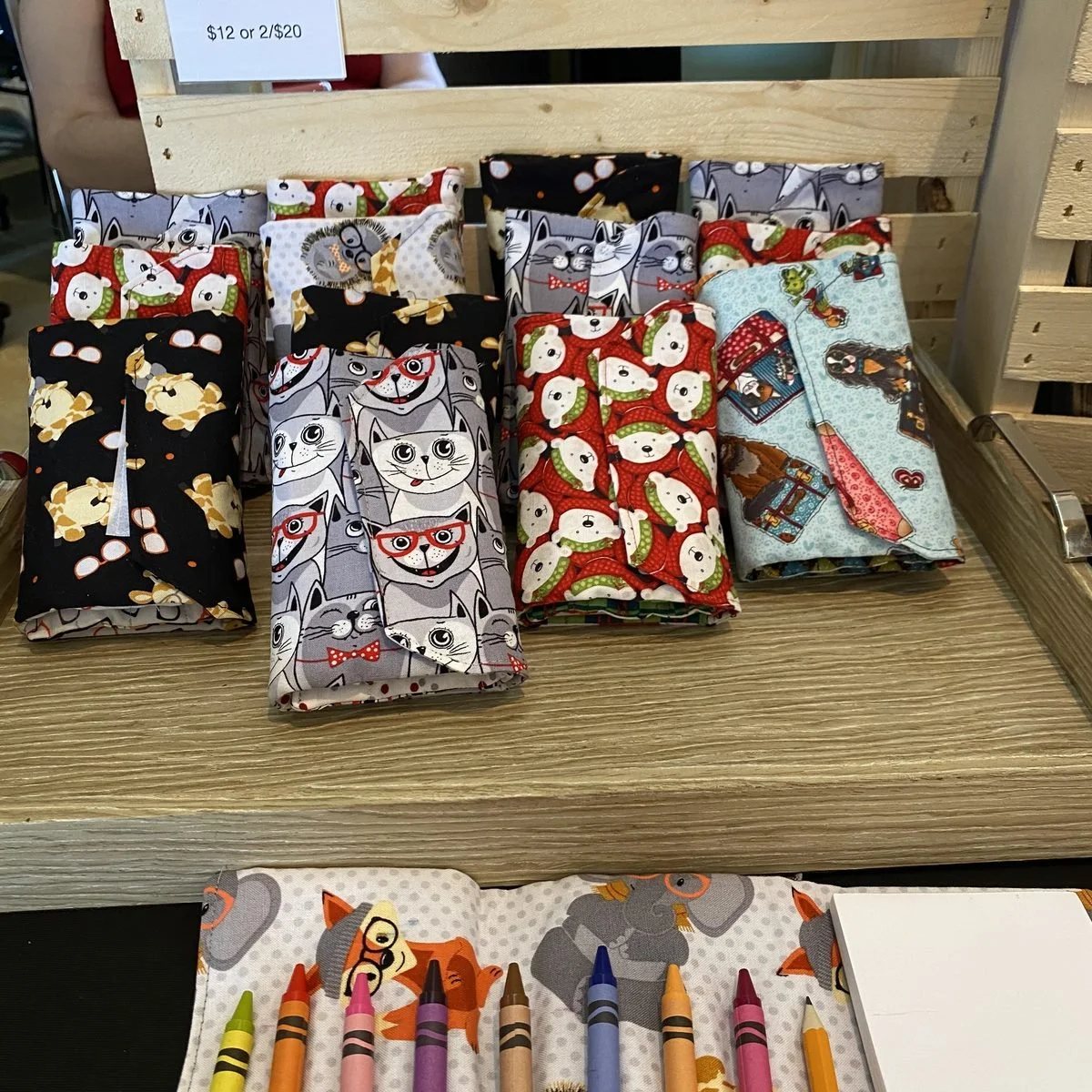 Folded fabric crayon wallets in cat, polar bear and giraffe prints, with one opened below to show crayons in its pockets