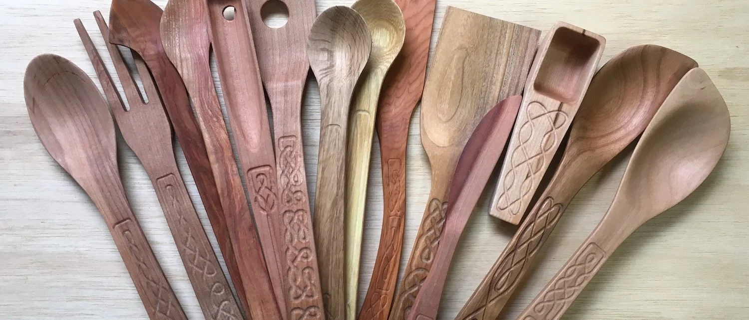 A fan of hand carved wooden spoons, forks, spatulas and scoops in different woods, each handle carved with a Celtic knot pattern