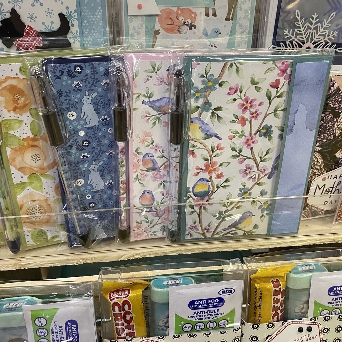 Notebook and pen sets in floral, bird and rabbit patterned covers, packaged and standing in a display rack
