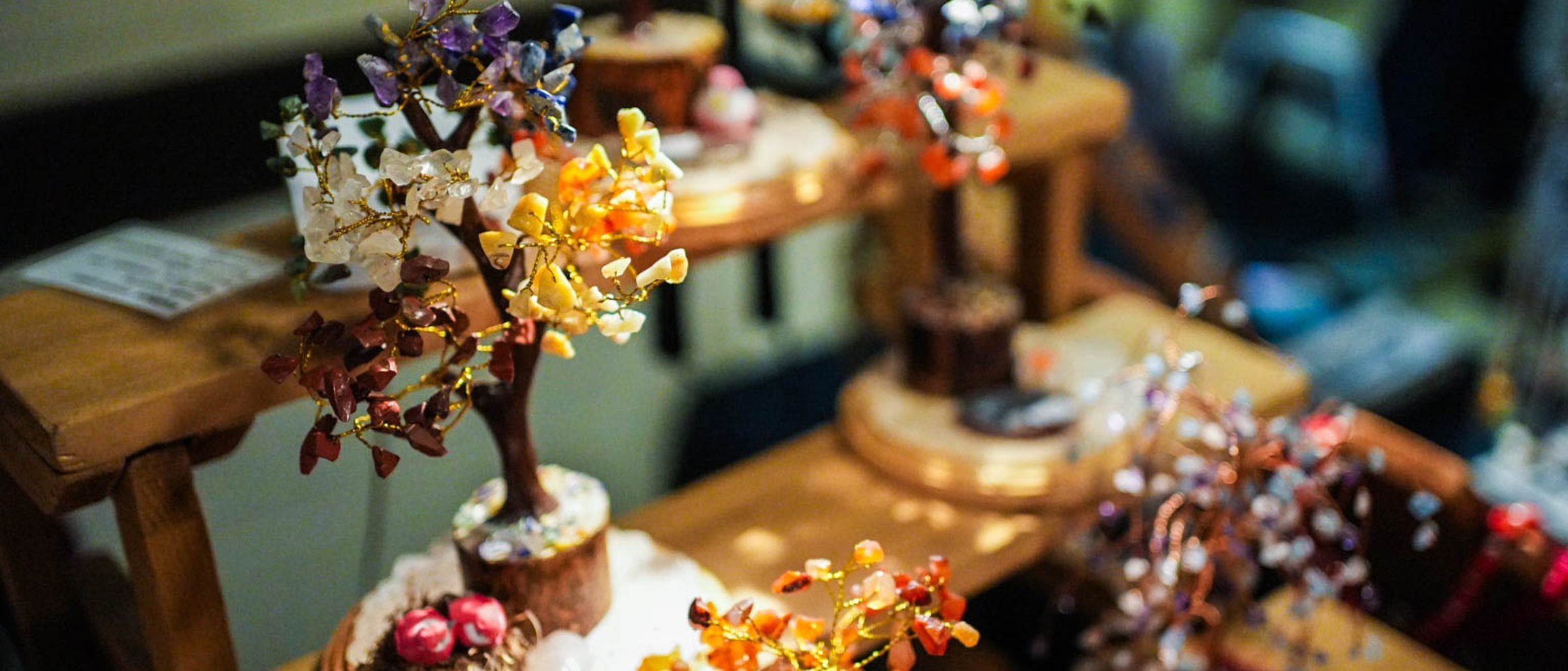 A row of small wire trees on wooden stands, their leaves made from chips of amethyst, citrine and other polished stones