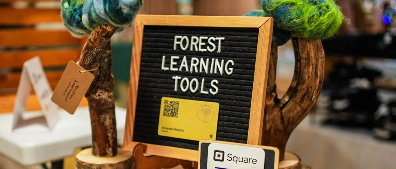 The Forest Learning Tools booth at the market, a letter board with the shop name flanked by wooden trees topped with green felted wool