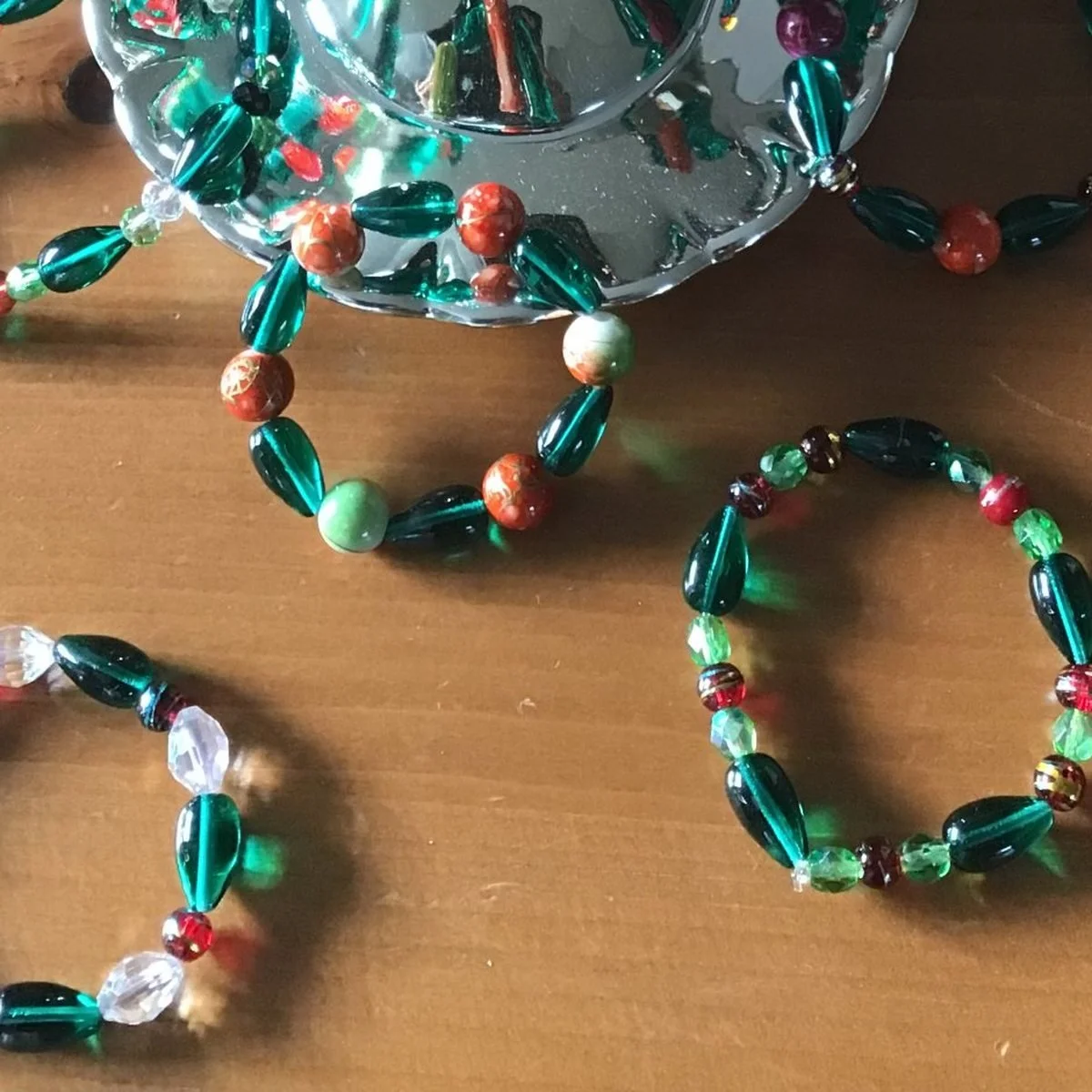 Beaded bracelets in dark green glass with red, orange and clear accents, laid out on a wooden table
