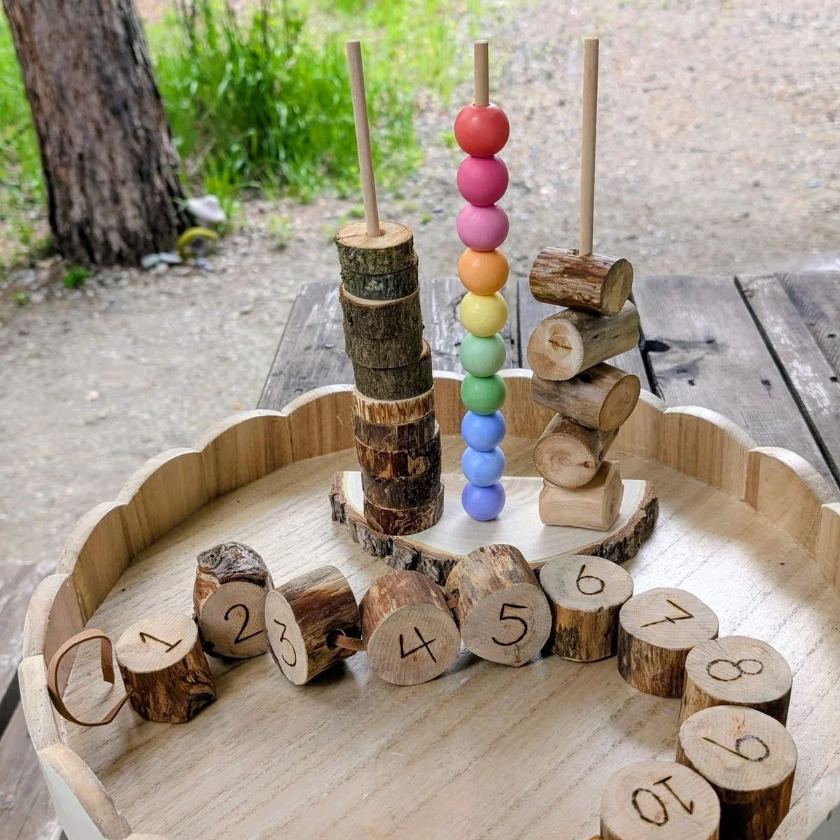 A wooden tray holding log rounds numbered one to ten, with stacking pegs and rainbow beads behind them