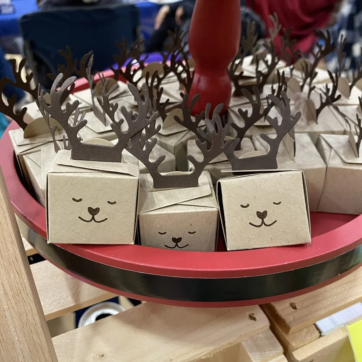 Small kraft paper treat boxes with drawn-on sleeping faces and cut paper antlers, arranged on a red and green tray