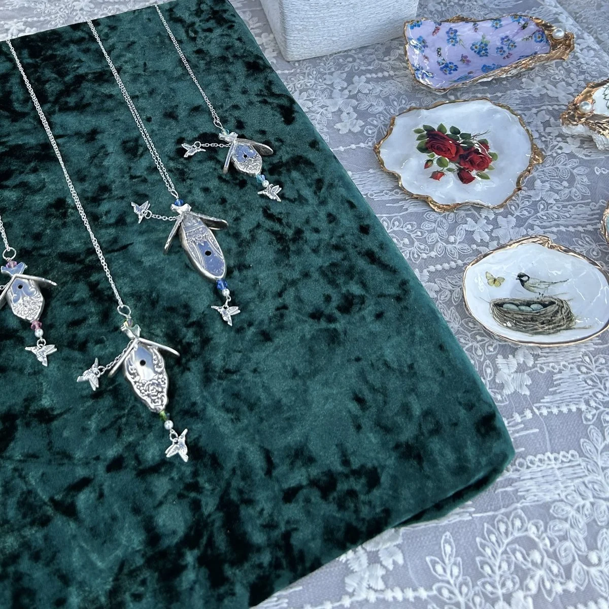 Four birdhouse pendants made from silver plated spoon handles, laid out on green velvet and hung with dragonfly and hummingbird charms