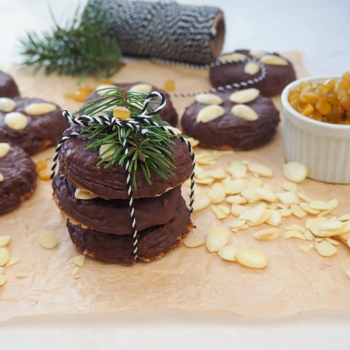 Chocolate glazed Lebkuchen topped with almonds, a stack tied with baker&rsquo;s twine and a sprig of fir, beside a dish of candied peel