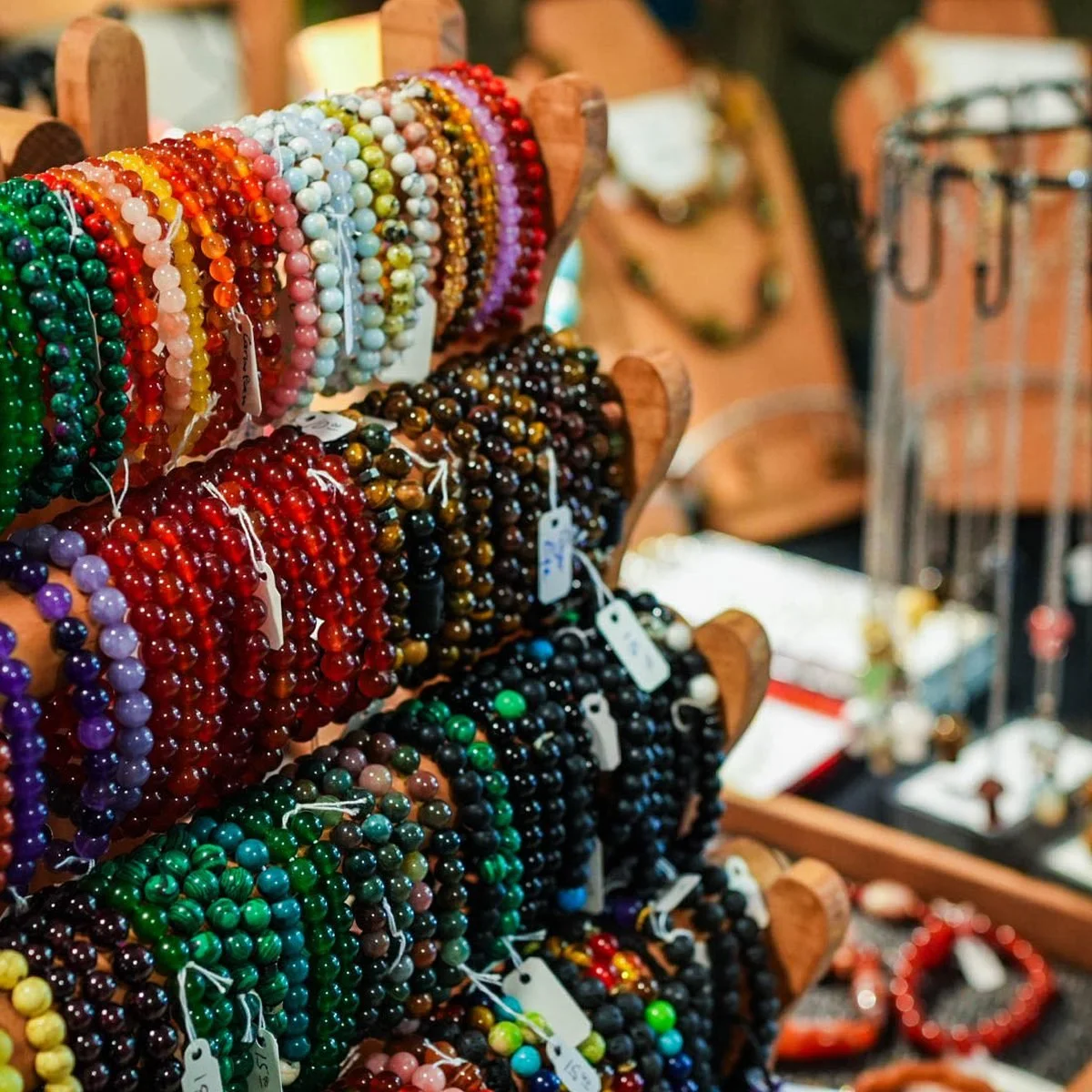 Rows of semi-precious stone bracelets on wooden stands, in green, red, blue and speckled grey